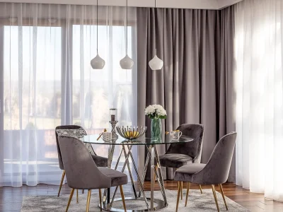 Stylowa jadalnia utrzymana w odcieniach szarości. Duże, werandowe oka udekorowane są szerokimi zasłonami z kolekcji Blackout oraz firanami woalowymi. Przy nowoczesnym, okrągłym stole wykonanym z metalu i szkła, stoją ekskluzywne krzesła tapicerowane aksamitną i miłą w dotyku tkaniną. Miękki dywan, oraz inne dodatki utrzymane w odcieniach szarości, uzupełniają całośc aranzacji. Nowoczesnośc miesza się tu z klasyczną elegancją.